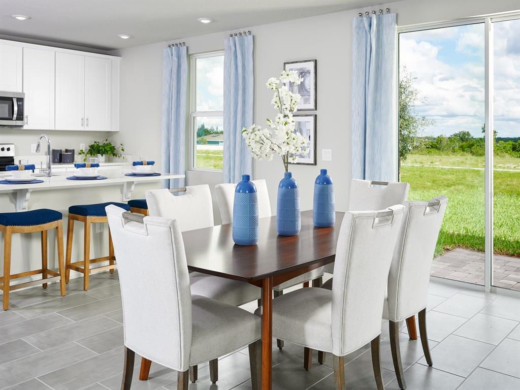 A dining area with a wooden table, white chairs, and blue vases near a kitchen — 2875 HORNBILL DRIVE, ST CLOUD, FL