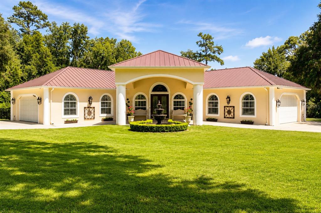 A single-story house with a metal roof, arched windows, and a central fountain in front — 22259 SKYVIEW CIRCLE, BROOKSVILLE, FL