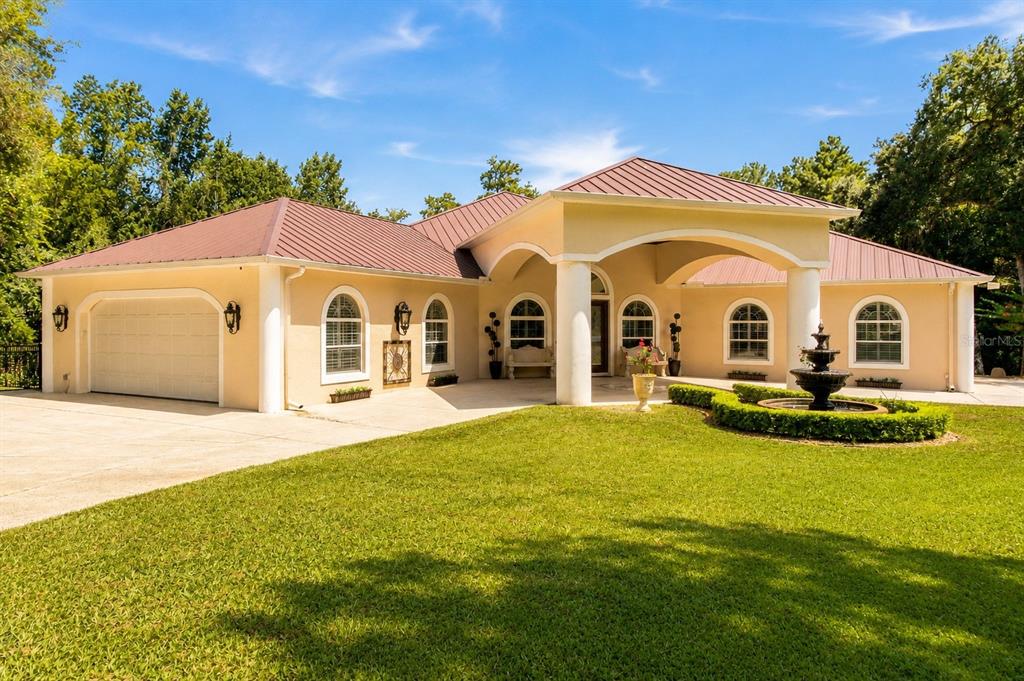 A single-story house with a metal roof, arched windows, and a front yard fountain — 22259 SKYVIEW CIRCLE, BROOKSVILLE, FL