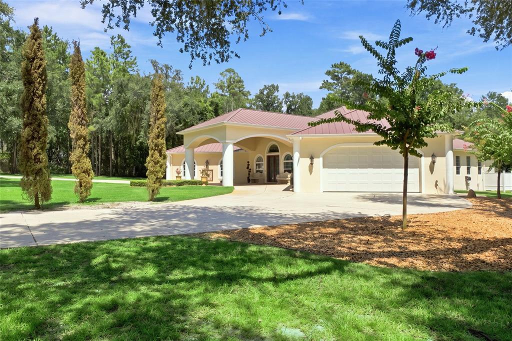 A single-story house with a metal roof, arched entryway, and a large concrete driveway — 22259 SKYVIEW CIRCLE, BROOKSVILLE, FL