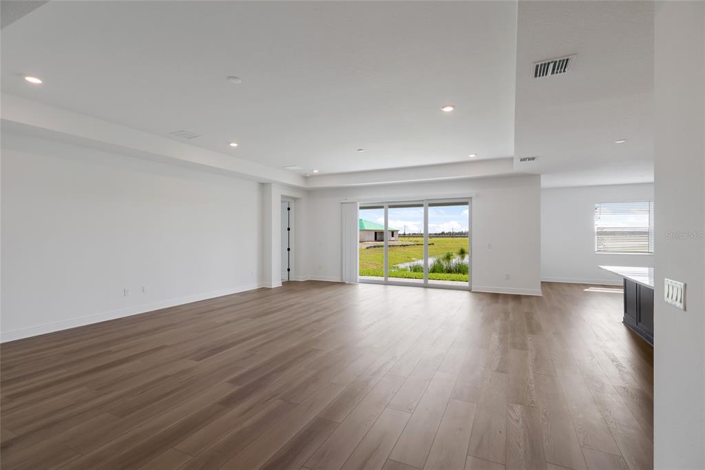 An empty living room with wood-look flooring, recessed lighting, and sliding glass doors to outdoors — 8924 DEEP HORIZON LOOP, PARRISH, FL