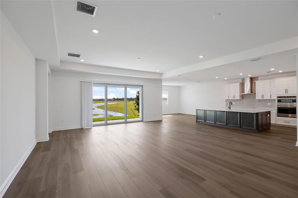 An open-concept living area with wood-look flooring, a kitchen island, and sliding glass doors — 8924 DEEP HORIZON LOOP, PARRISH, FL