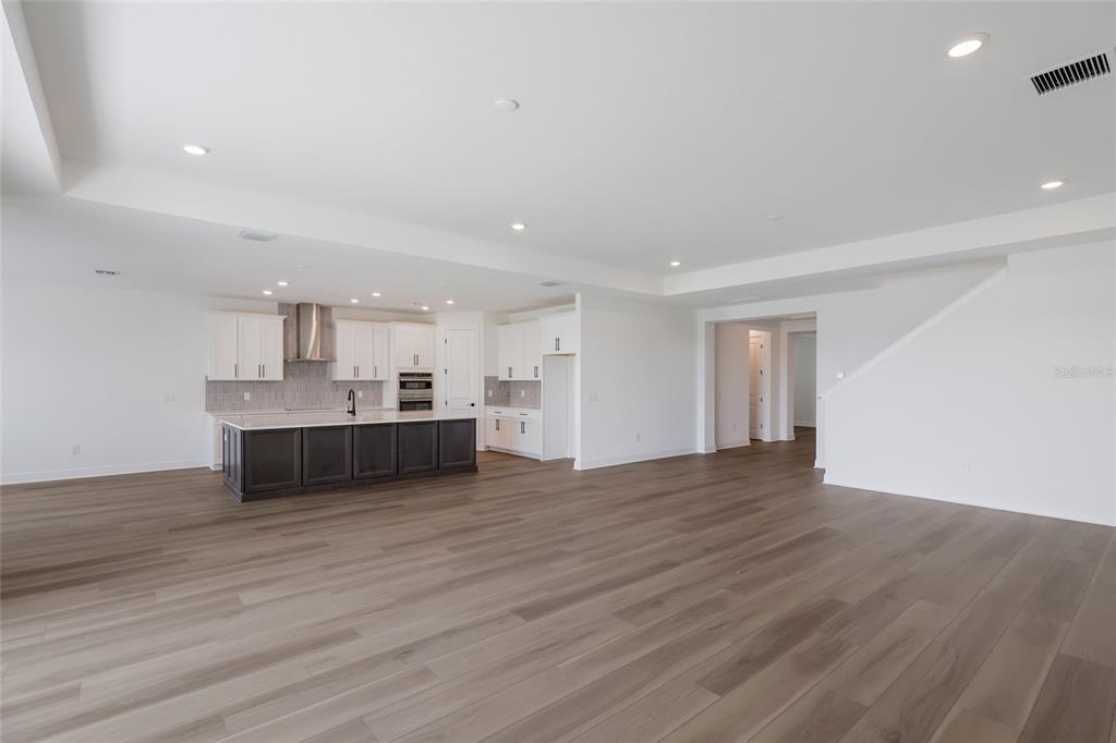 A spacious open-concept kitchen and living area featuring dark cabinetry, white countertops, and wood flooring — 8924 DEEP HORIZON LOOP, PARRISH, FL
