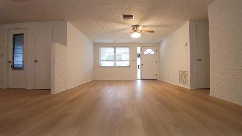 An open-concept living area features light wood-look flooring, a ceiling fan, and a white front door — 2109 SHANNON DRIVE, HOLIDAY, FL