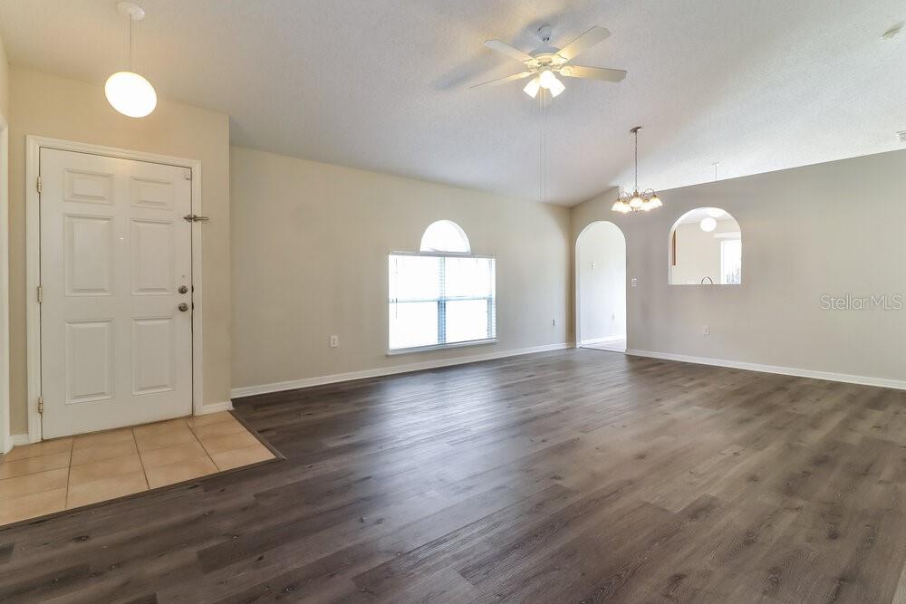 An open living area features light-colored walls, wood-look flooring, a ceiling fan, and arched doorways — 6452 TABOGI TRAIL, WESLEY CHAPEL, FL