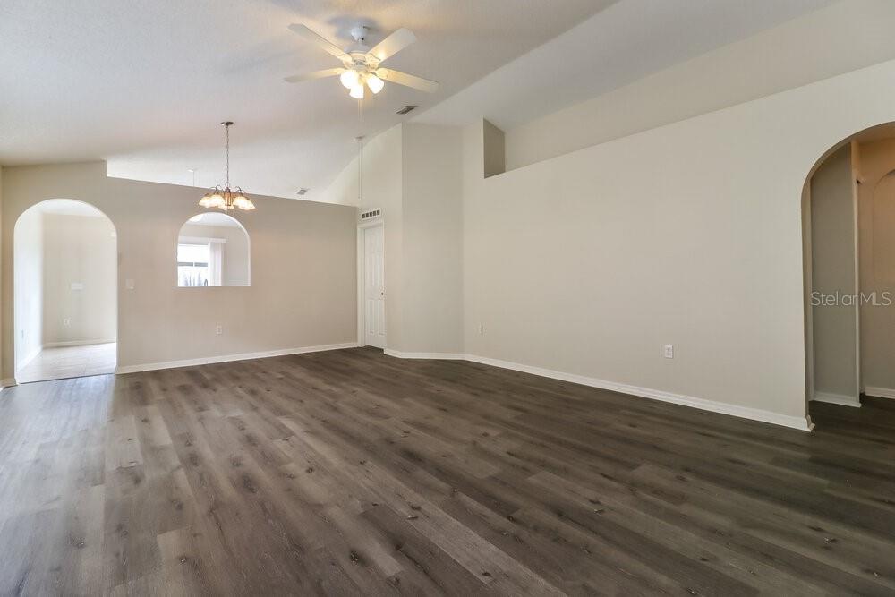 A spacious living room features vaulted ceilings, light-colored walls, and dark wood-look flooring — 6452 TABOGI TRAIL, WESLEY CHAPEL, FL