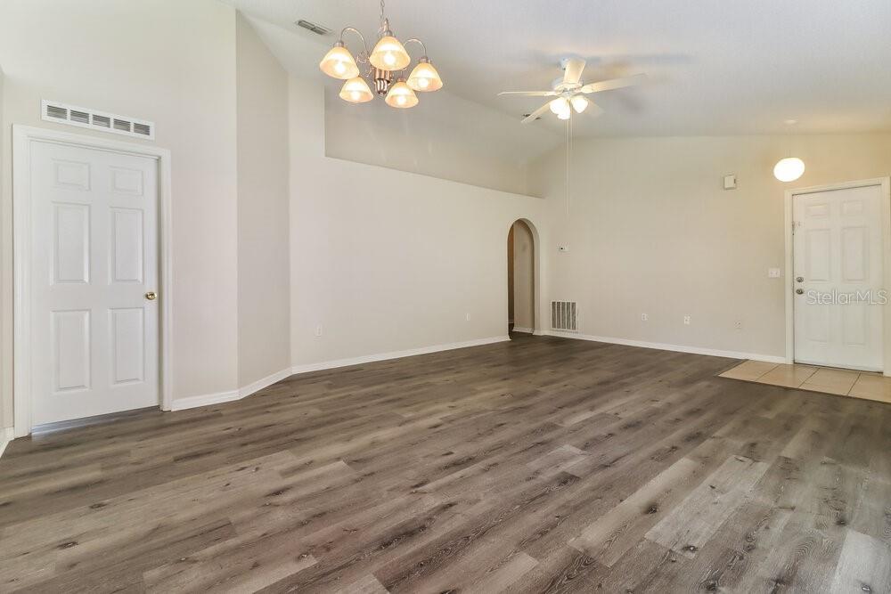 An empty room with wood-look flooring, a vaulted ceiling, a chandelier, and a ceiling fan — 6452 TABOGI TRAIL, WESLEY CHAPEL, FL