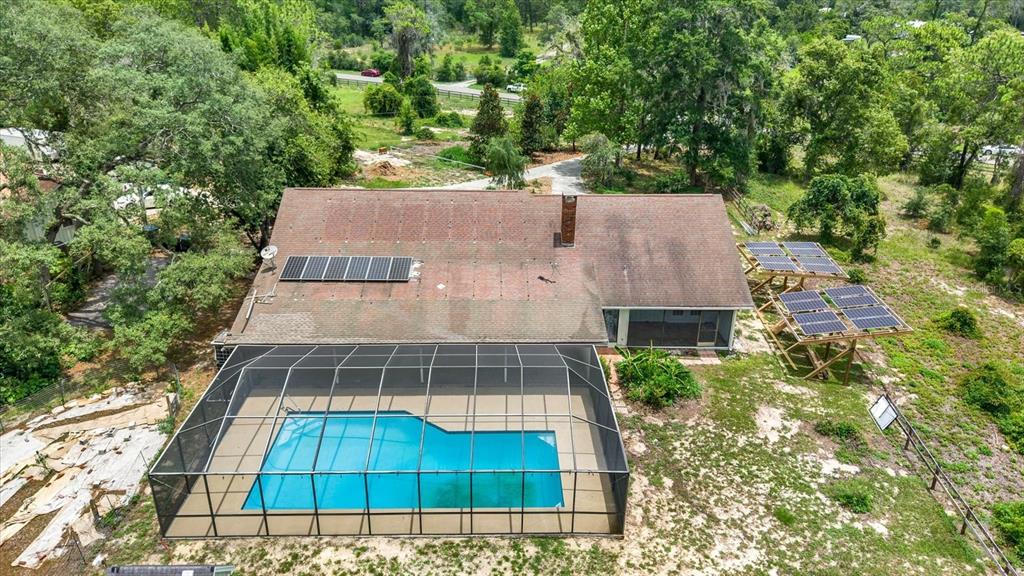 An aerial view shows a house with a screened-in pool and ground-mounted solar panels — 11251 SALINA STREET, BROOKSVILLE, FL