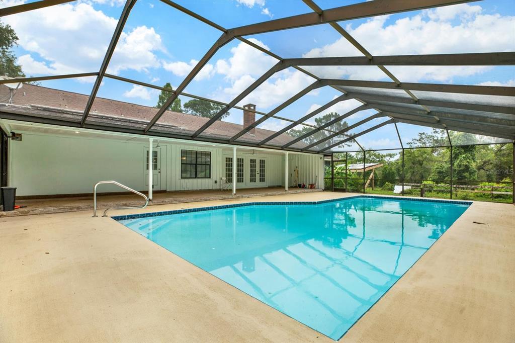 A swimming pool sits on a concrete patio enclosed by a large metal screen cage — 11251 SALINA STREET, BROOKSVILLE, FL