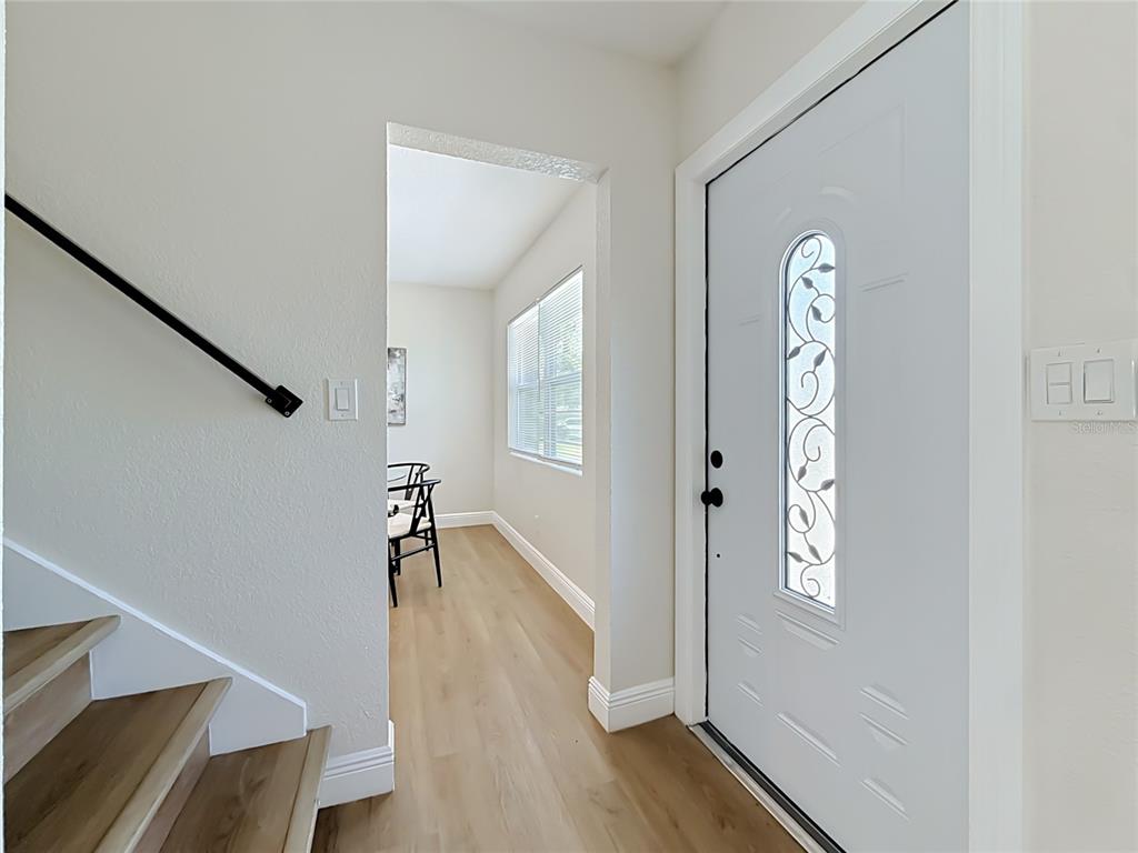 An entryway features light wood flooring, a white front door, and stairs with a black railing — 8718 94TH ST, SEMINOLE, FL