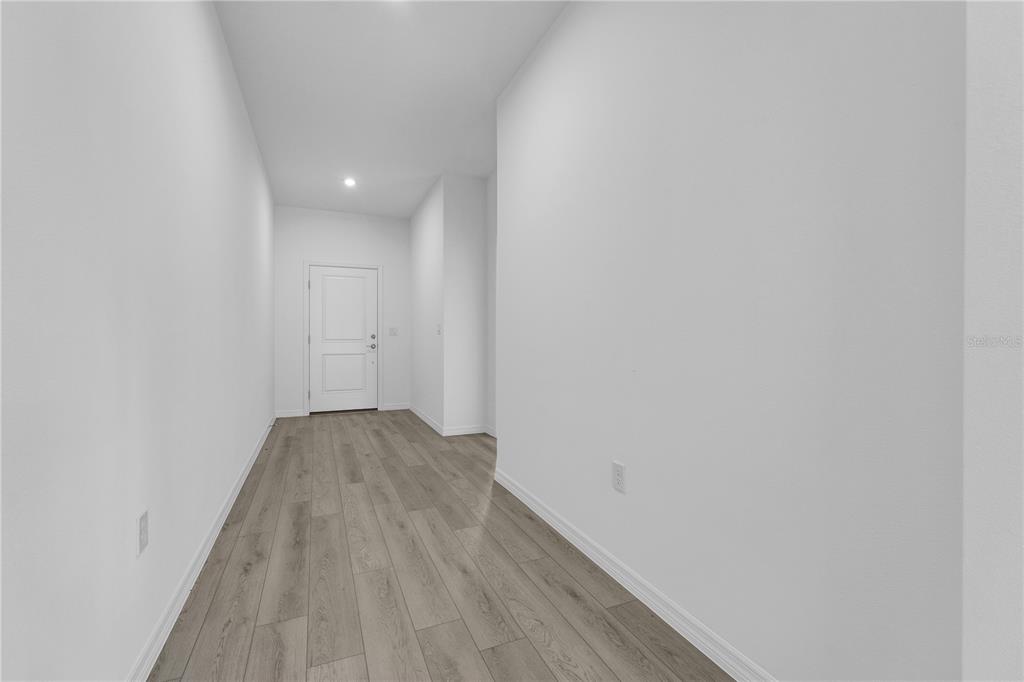 A narrow, empty hallway with white walls and light-colored wood-look flooring leads to a door — 1112 BANFF DRIVE NE, PALM BAY, FL
