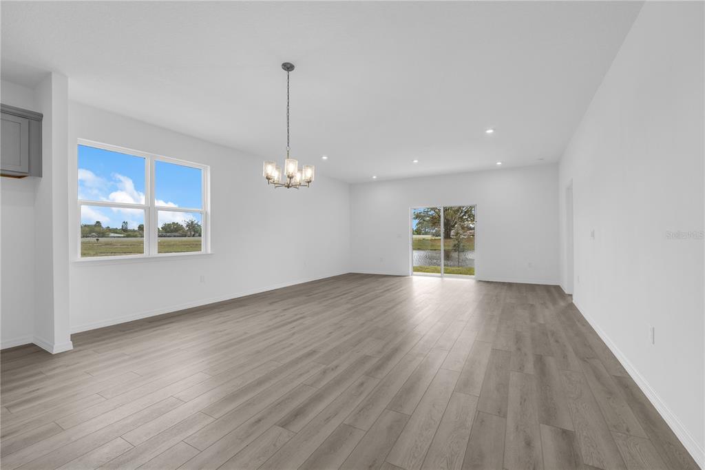 A spacious, unfurnished living area features white walls, light wood-look flooring, a chandelier, and sliding doors — 1112 BANFF DRIVE NE, PALM BAY, FL