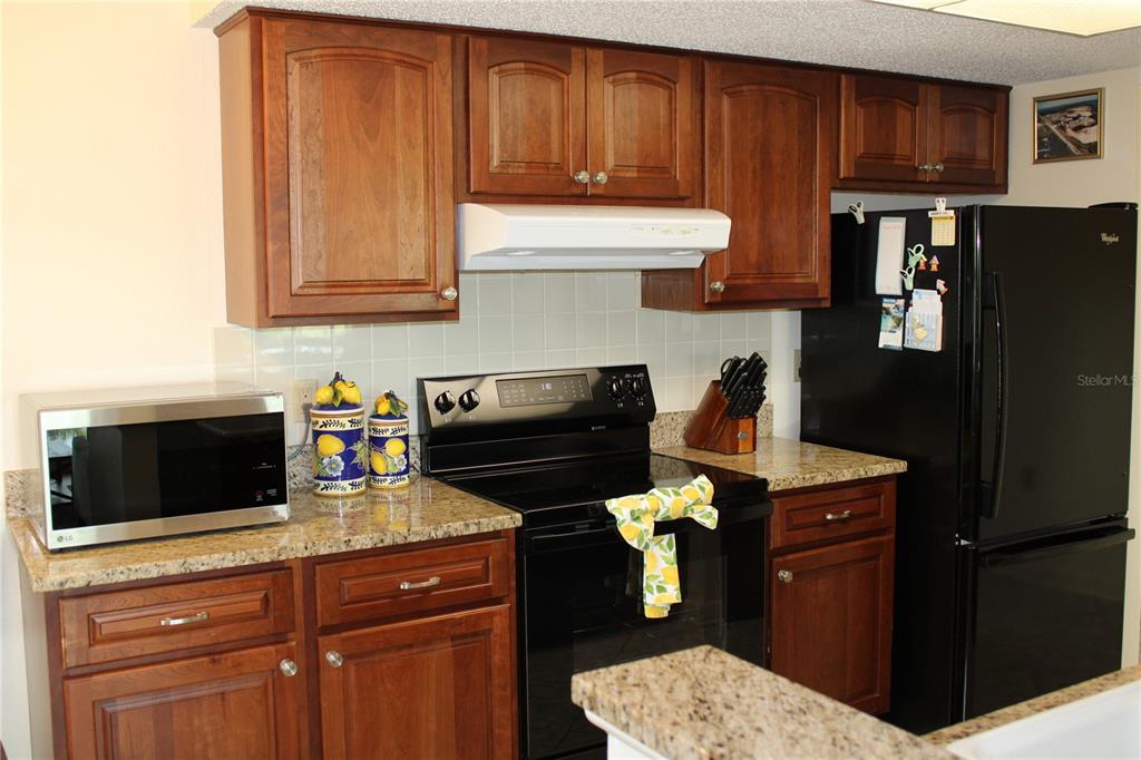 A kitchen features wood cabinets, granite countertops, a black stove, and a white tile backsplash — 327 108TH STREET W UNIT 327, BRADENTON, FL