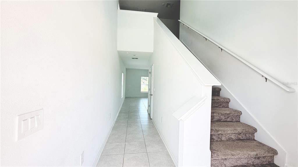 A bright entryway features white walls, tiled flooring, and a carpeted staircase with a railing — 1033 WATERFALL BOULEVARD, DAVENPORT, FL