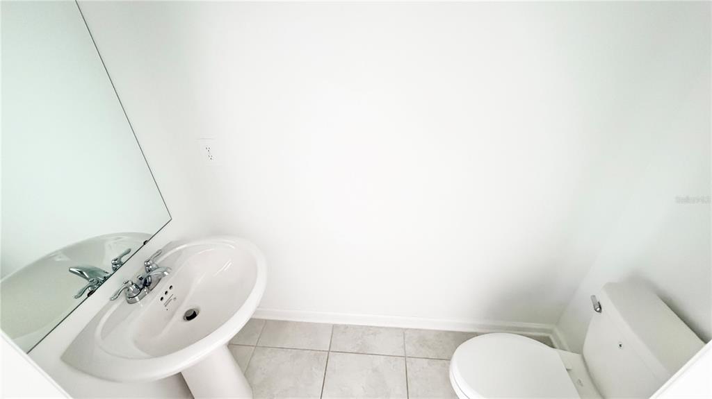 A small bathroom featuring a white pedestal sink, a toilet, and light-colored floor tiles — 1033 WATERFALL BOULEVARD, DAVENPORT, FL