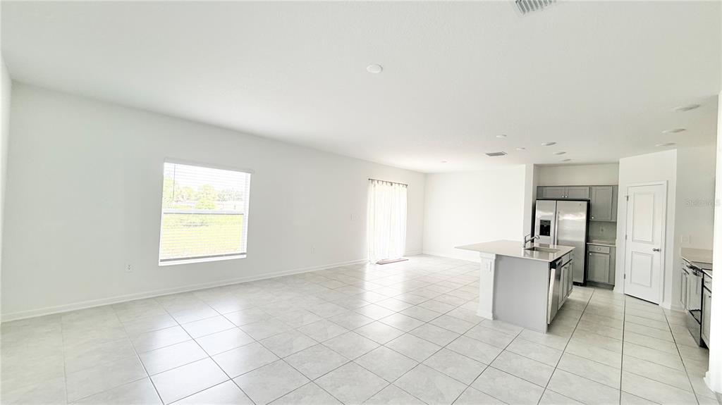 An open-concept kitchen and living area with white walls, tile flooring, and stainless steel appliances — 1033 WATERFALL BOULEVARD, DAVENPORT, FL