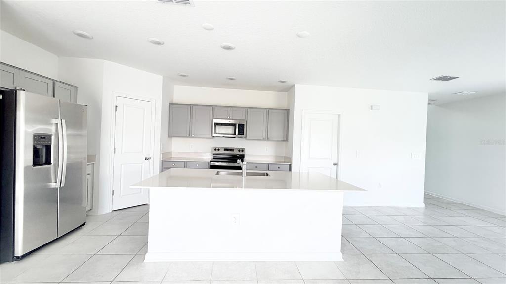 A kitchen features a white island, stainless steel appliances, and gray cabinets against white walls — 1033 WATERFALL BOULEVARD, DAVENPORT, FL
