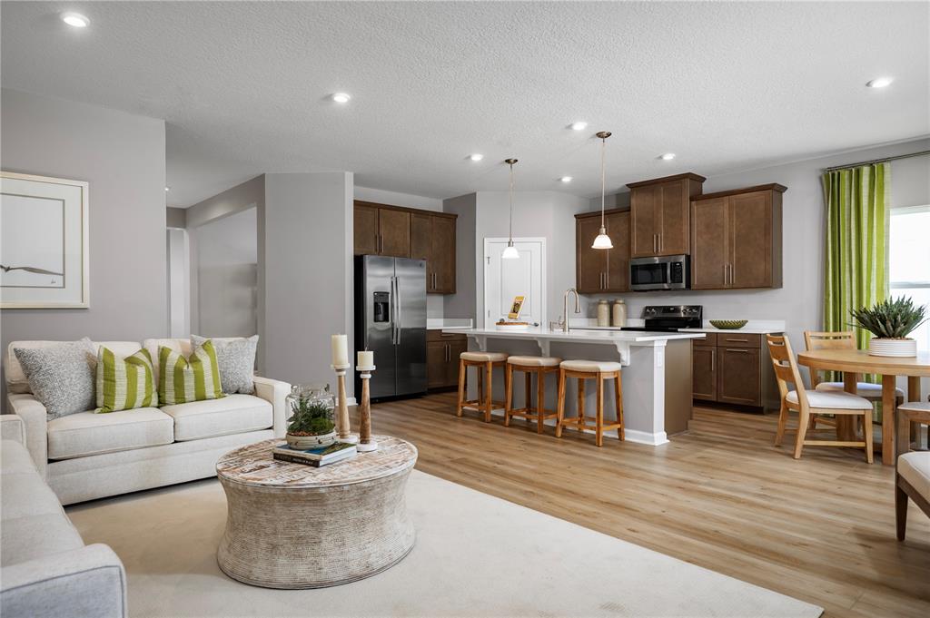 An open-concept kitchen and living area features wood cabinets, stainless appliances, and light wood flooring — 1016 OCEAN LODGE ROAD, LADY LAKE, FL