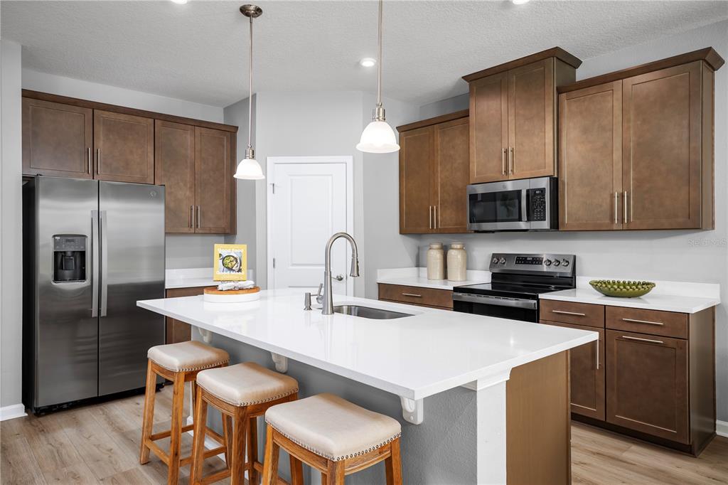 A modern kitchen features brown wood cabinets, white countertops, a central island, and stainless appliances — 1016 OCEAN LODGE ROAD, LADY LAKE, FL