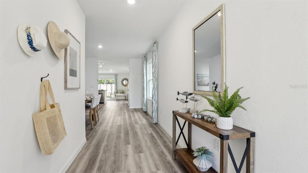 A bright entryway features wood-look flooring, a console table, a wall mirror, and wall hooks — 11952 NOBLE CHASE PATH, DADE CITY, FL