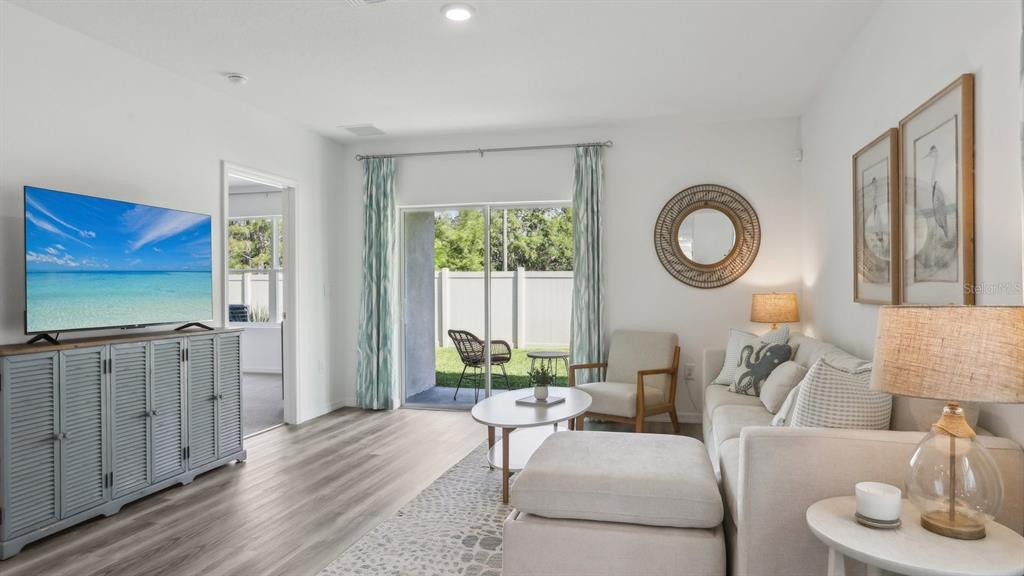A living room features a grey media console, a beige sectional, and sliding glass doors — 11952 NOBLE CHASE PATH, DADE CITY, FL