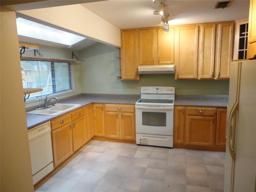 A kitchen features light wood cabinets, laminate countertops, a white stove, and a double sink — 7823 SW 9TH PLACE, GAINESVILLE, FL