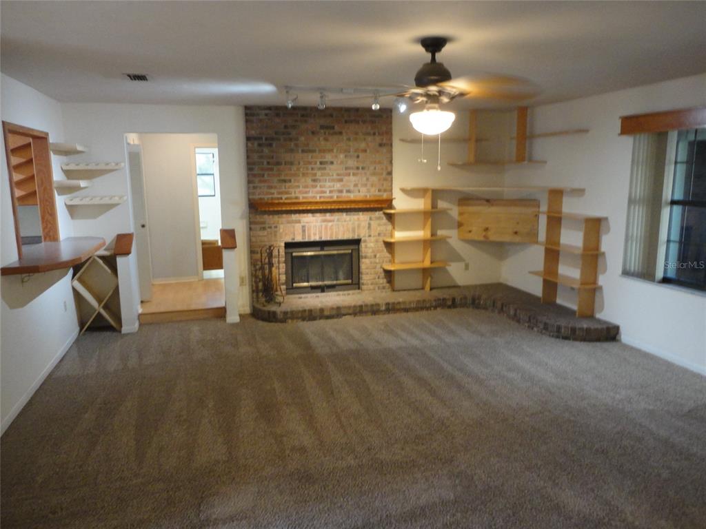 A living room features a brick fireplace, built-in wooden shelving, and wall-to-wall carpeting — 7823 SW 9TH PLACE, GAINESVILLE, FL