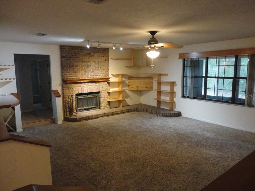 A living room features a brick fireplace, built-in wooden shelving, and a ceiling fan — 7823 SW 9TH PLACE, GAINESVILLE, FL