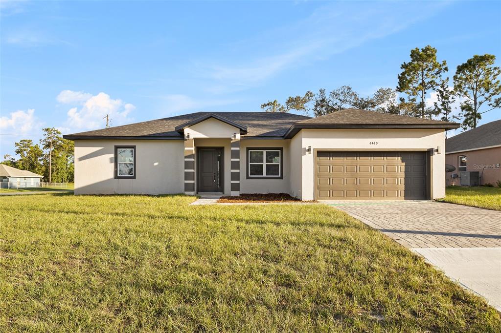 A single-story house with a beige stucco exterior, a two-car garage, and a paved driveway — 6460 SW 129 LOOP, OCALA, FL