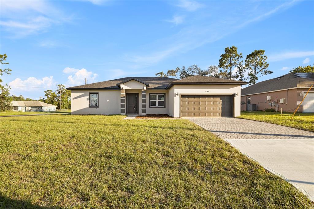 A single-story house with a beige stucco exterior, a two-car garage, and a paved driveway — 6460 SW 129 LOOP, OCALA, FL