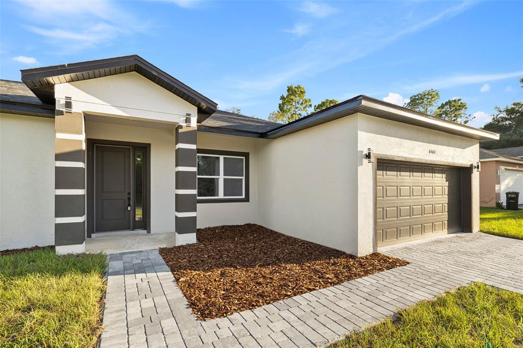 A single-story house exterior features a paved walkway, brown mulch, and a two-car garage — 6460 SW 129 LOOP, OCALA, FL