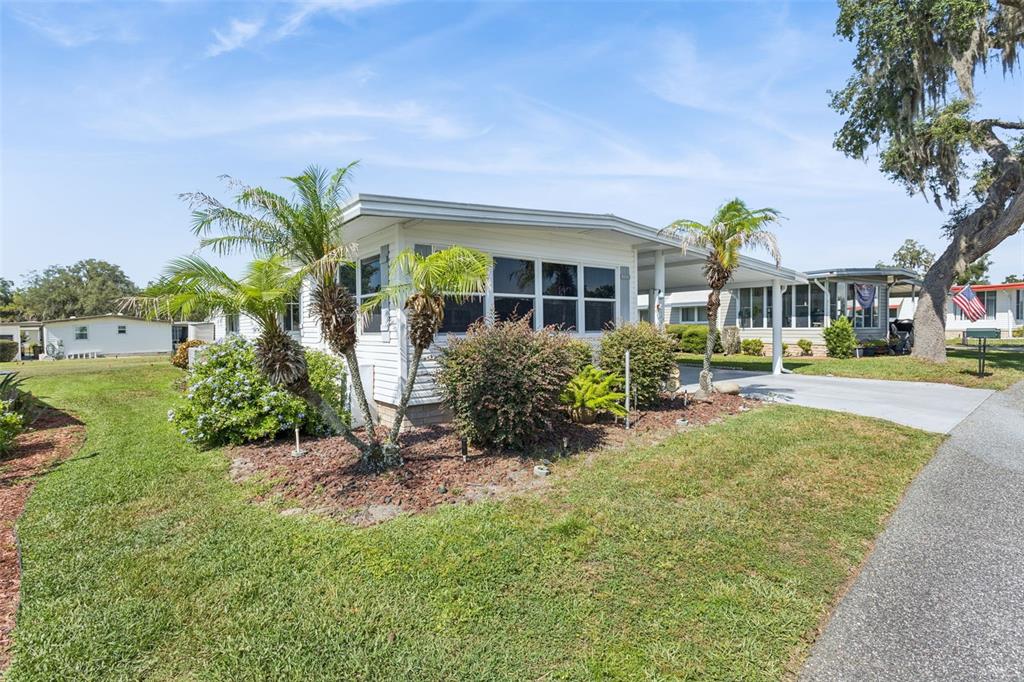 A white mobile home with a carport and palm trees sits on a grassy lot — 137 JACARANDA DRIVE, LEESBURG, FL