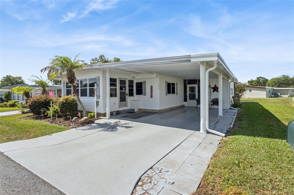 A white single-story manufactured home with a carport and a concrete driveway — 137 JACARANDA DRIVE, LEESBURG, FL