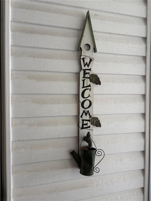 A vertical wooden welcome sign with a decorative metal watering can hangs on white siding — 137 JACARANDA DRIVE, LEESBURG, FL