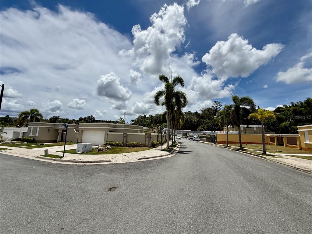 A paved street curves past residential buildings and palm trees under a cloudy blue sky — 834 CALLE 3 UNIT B13, GUAYNABO, PR