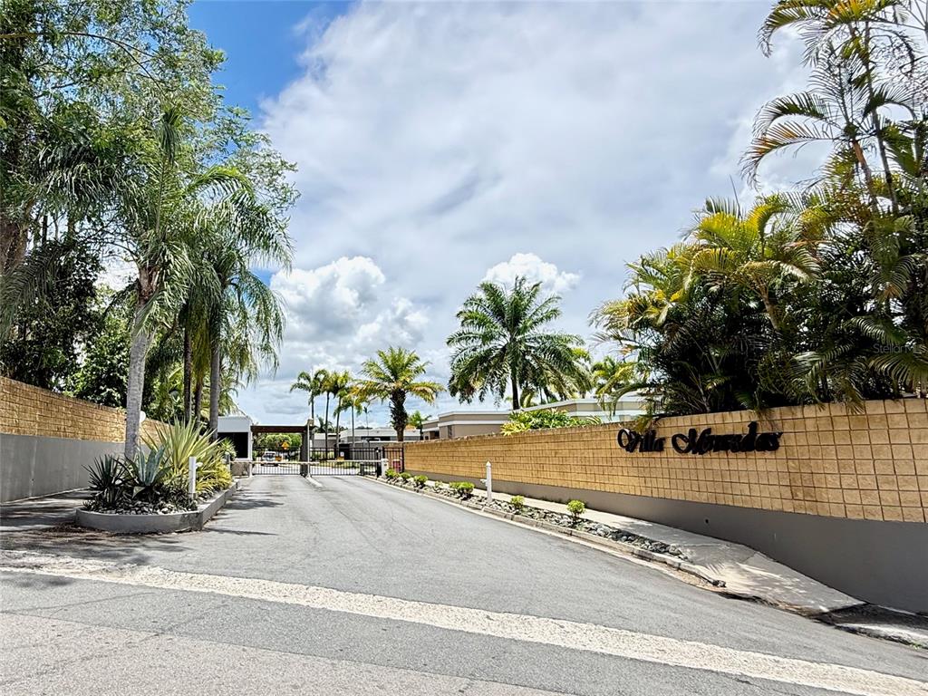 A paved road leads to the gated entrance of a residential community with palm trees — 834 CALLE 3 UNIT B13, GUAYNABO, PR