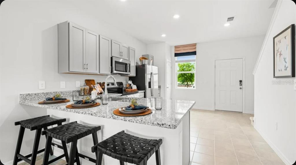 A kitchen features light gray cabinets, granite countertops, and a breakfast bar with three stools — 667 NESS ISLAND DRIVE UNIT 0, MOUNT DORA, FL