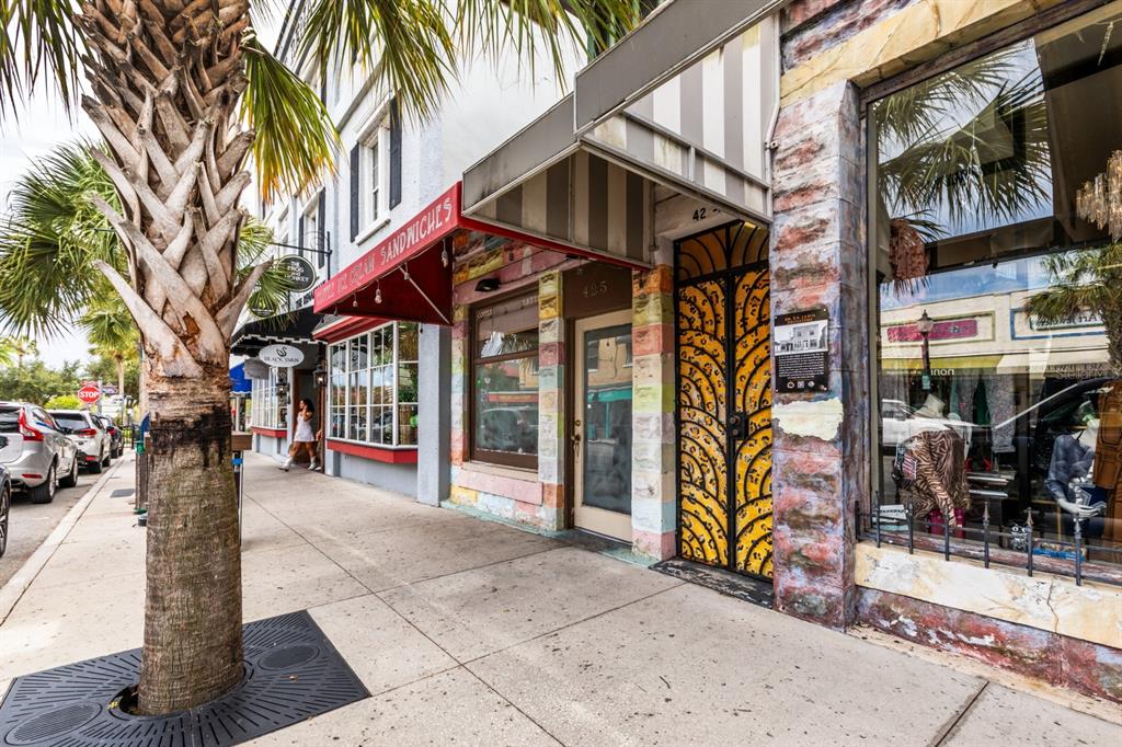 A sidewalk view of a storefront with a colorful facade, striped awning, and palm tree — 427 N DONNELLY STREET, MOUNT DORA, FL