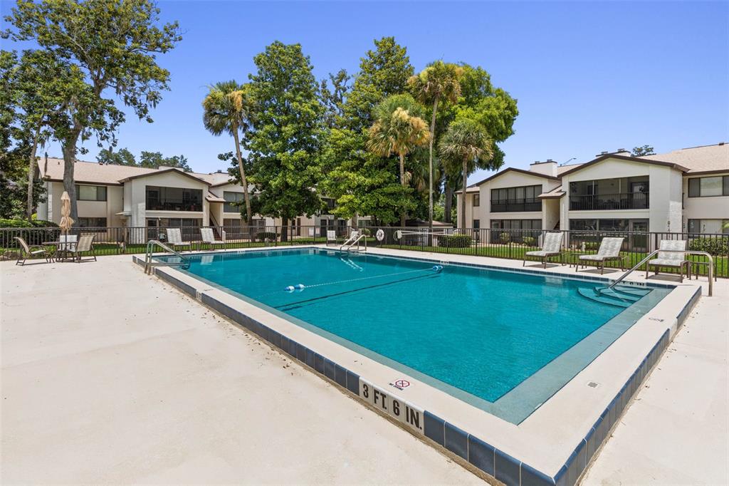A rectangular swimming pool sits in front of multi-story apartment buildings with palm trees — 1 TOMOKA OAKS BOULEVARD UNIT 137, ORMOND BEACH, FL