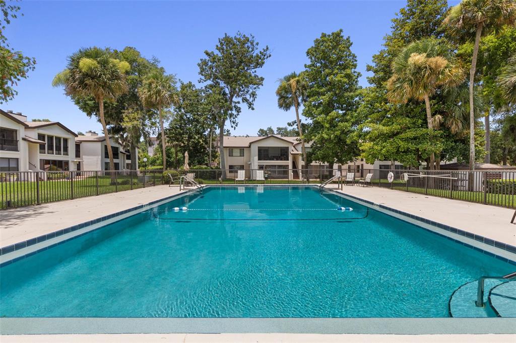 A rectangular swimming pool is surrounded by a concrete deck, metal fencing, and palm trees — 1 TOMOKA OAKS BOULEVARD UNIT 137, ORMOND BEACH, FL