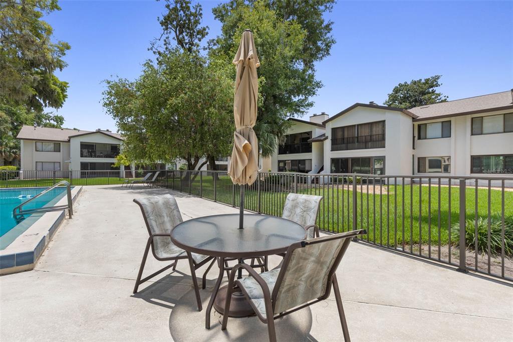 A patio with a glass-top table and chairs sits beside a swimming pool and apartments — 1 TOMOKA OAKS BOULEVARD UNIT 137, ORMOND BEACH, FL