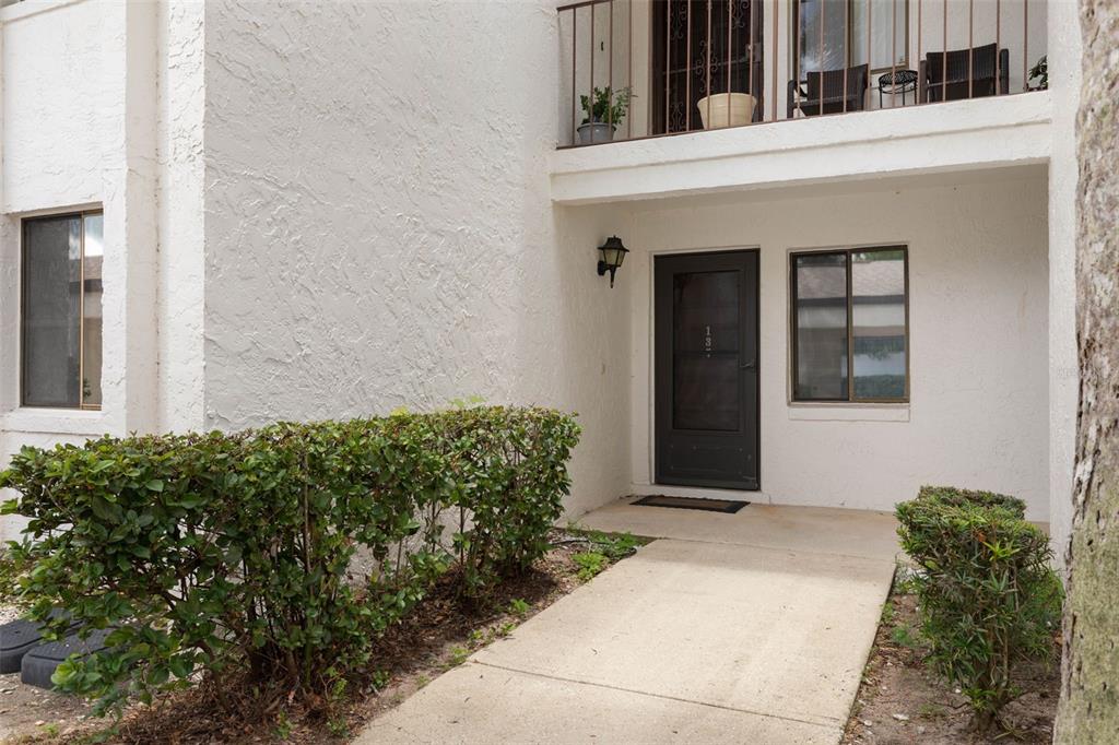 A concrete walkway leads to the front entrance of a white stucco building with landscaping — 1 TOMOKA OAKS BOULEVARD UNIT 137, ORMOND BEACH, FL
