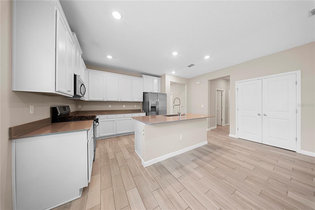 A kitchen features white cabinets, a central island with a sink, and light wood-look flooring — 136 MONTSERRAT DRIVE, ST AUGUSTINE, FL