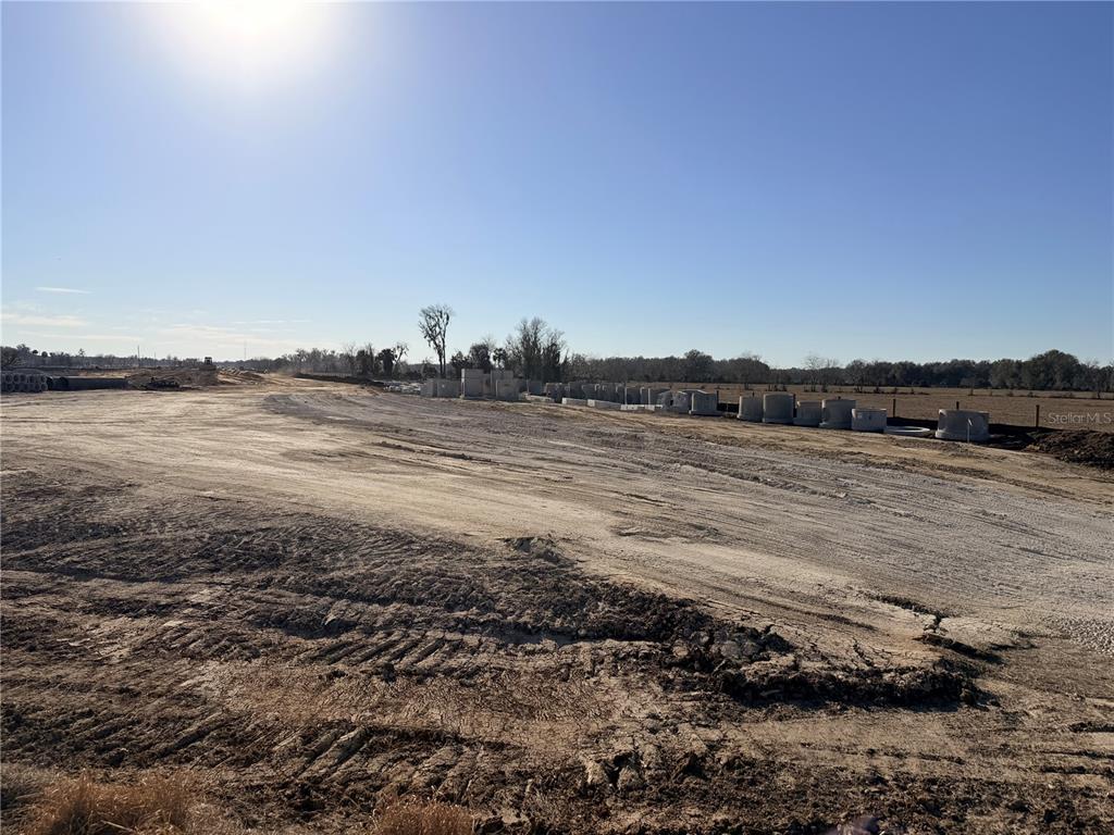 A dirt construction site features scattered concrete drainage pipes under a clear blue sky — CR 523, COLEMAN, FL