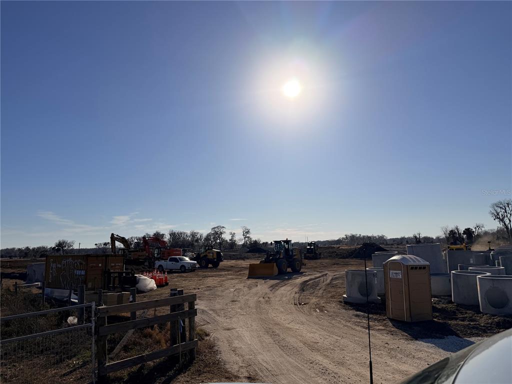 A construction site features heavy machinery, concrete pipes, and a portable restroom under a bright sun — CR 523, COLEMAN, FL