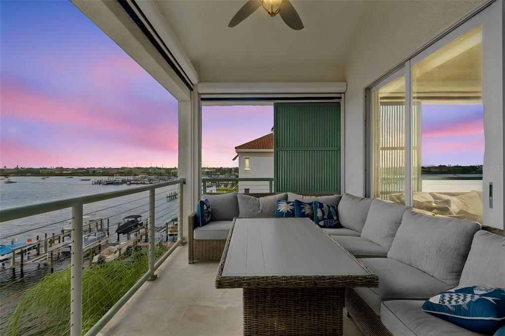 A covered balcony features a wicker sectional sofa, a dining table, and waterfront views — 1038 BELLASOL WAY UNIT 403, APOLLO BEACH, FL