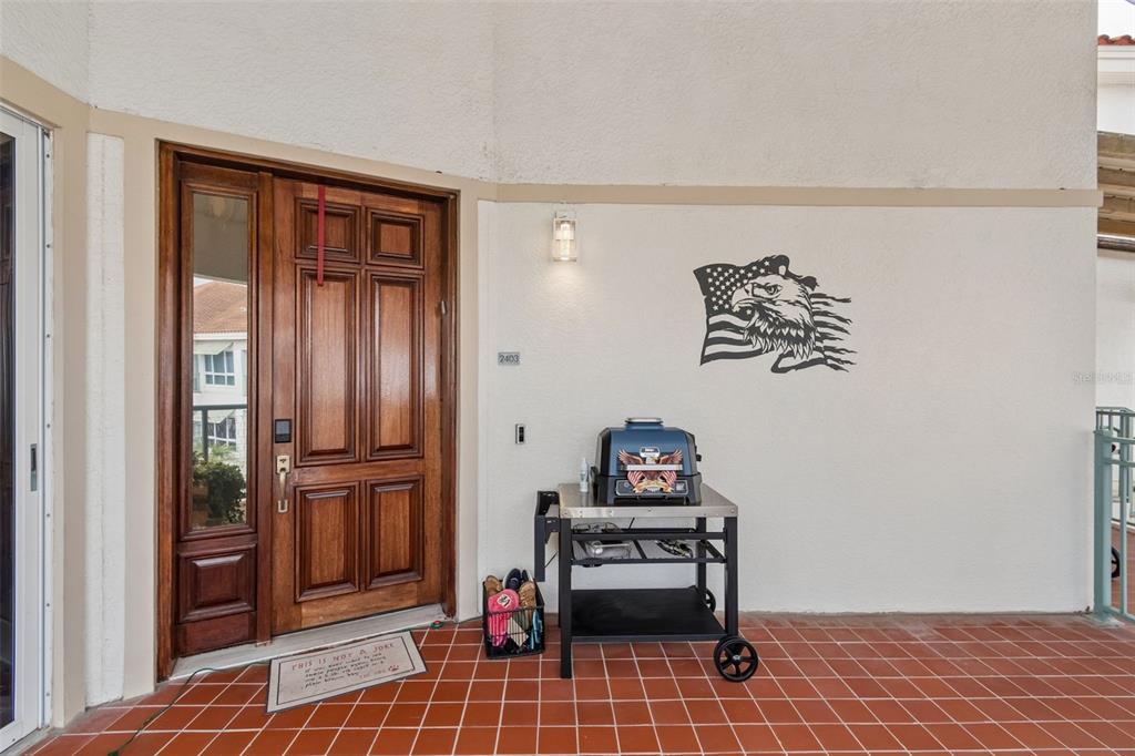 A wooden front door and a grill on a cart sit on a tiled patio — 1038 BELLASOL WAY UNIT 403, APOLLO BEACH, FL