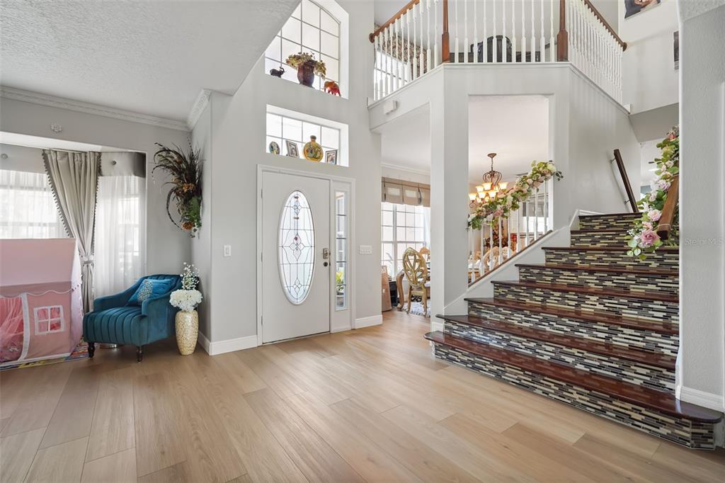 A bright entryway features light wood flooring, a staircase with tiled risers, and a front door — 2491 PRAIRIE VIEW DRIVE, WINTER GARDEN, FL