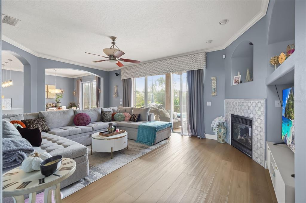 A living room features a gray sectional sofa, a fireplace with patterned tile, and wood flooring — 2491 PRAIRIE VIEW DRIVE, WINTER GARDEN, FL