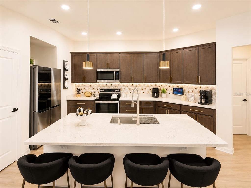 A modern kitchen features dark wood cabinets, a large white island, and black bar stools — 1743 WILSON PRAIRIE CIRCLE, GROVELAND, FL